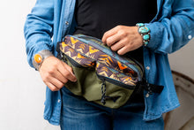 Load image into Gallery viewer, Person wearing a blue button up shirt with blue jeans is unzipping a Pendleton patterned fanny pack they are wearing
