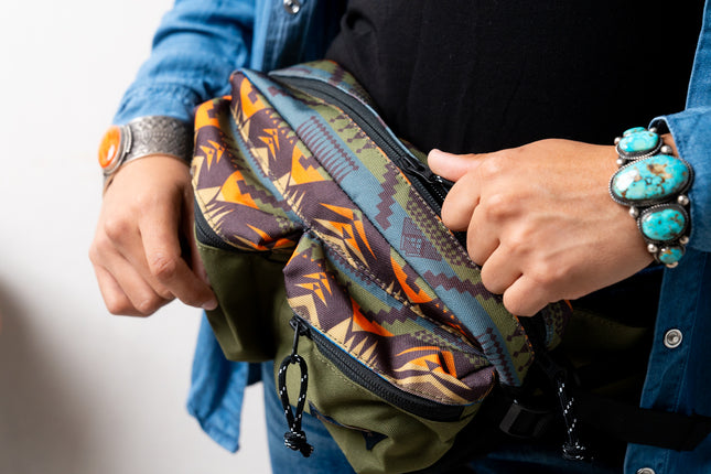 Person holding a Pendleton patterned bag with colorful designs, wearing a blue jacket and turquoise bracelet.