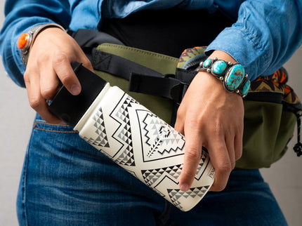 Close up of a person holding a white Pendleton patterned mug at waist level with a green fanny pack behind the mug