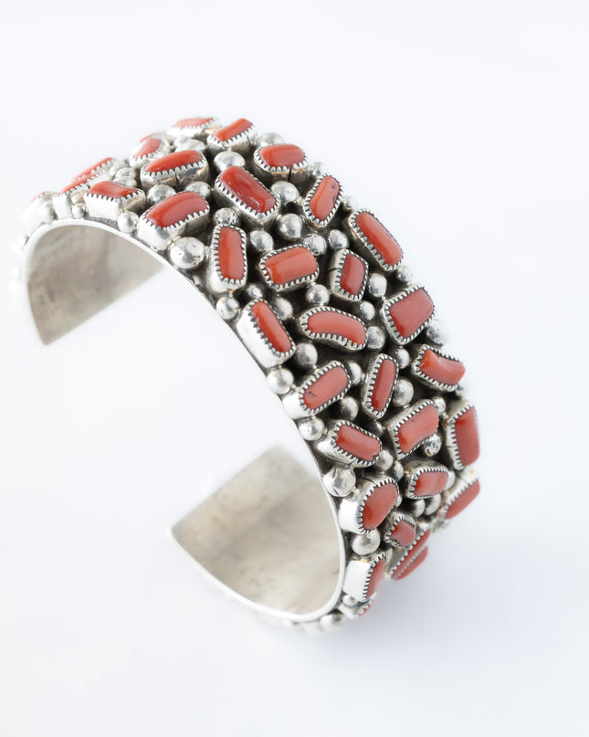 Navajo sterling silver, coral cluster bracelet on top of a white background.