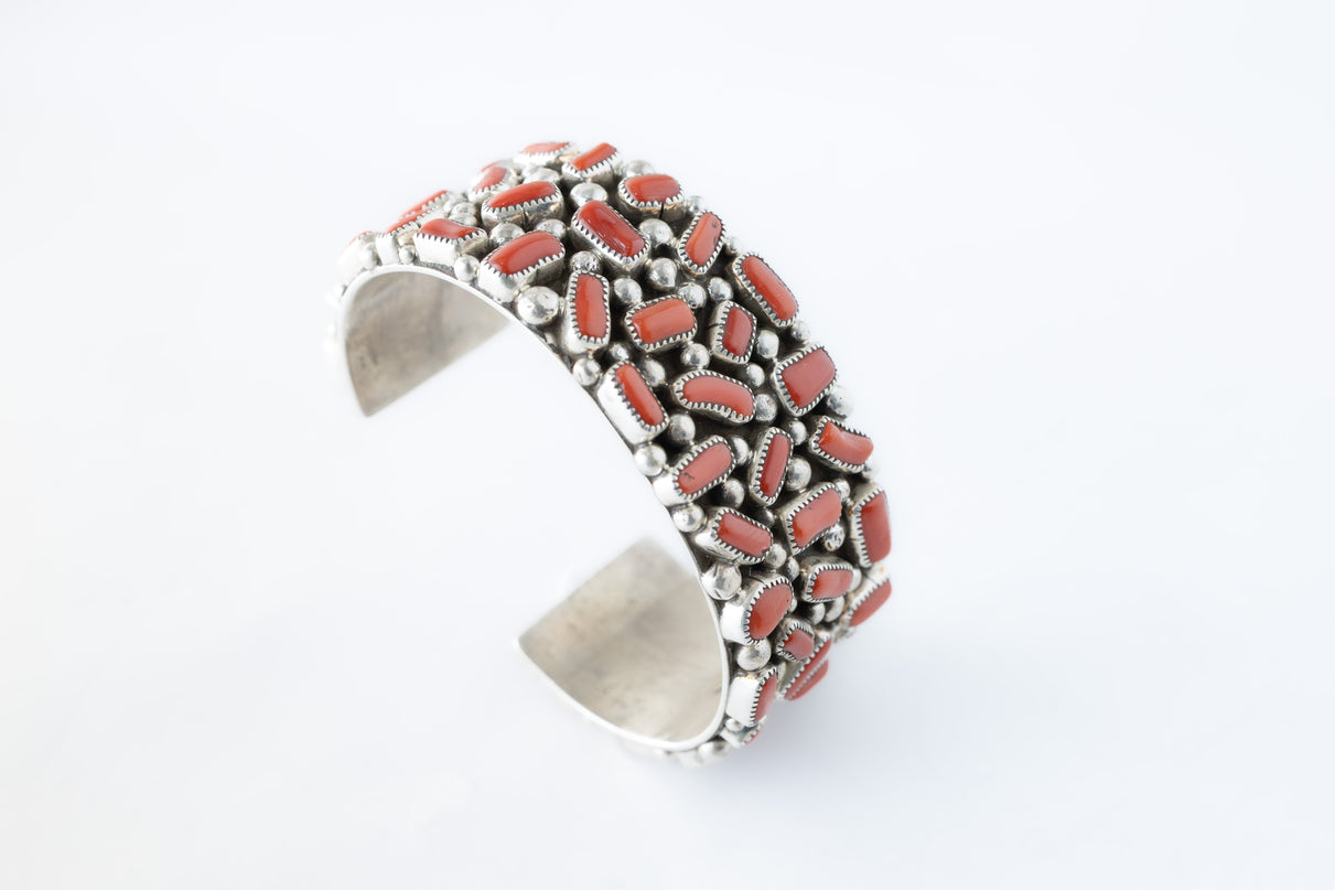 Navajo sterling silver, coral cluster bracelet on top of a white background.