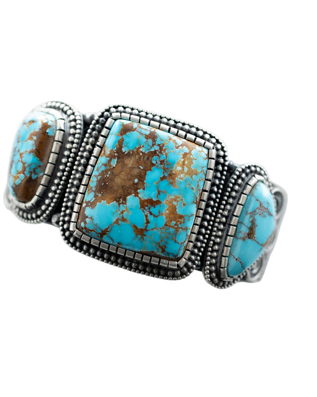 Top of a silver bracelet with three Royston Turquoise stones, by Navajo Silversmith Matthew Charley, with a solid white background. 