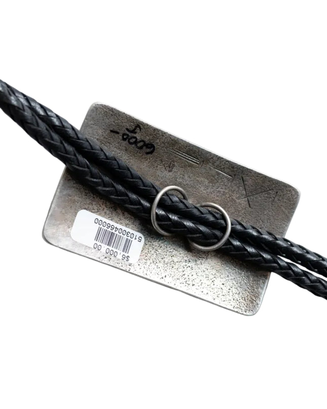 Black leather cord being looped through two silver circular loops on the back of a rectangular bolo tie