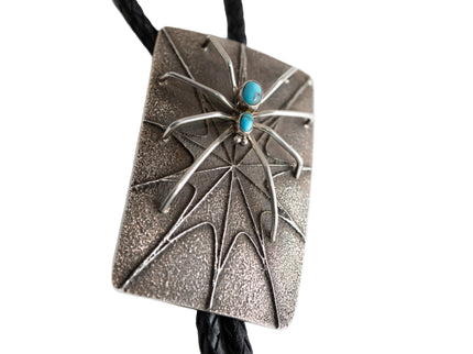 Silver spider rectangular bolo tie with two turquoise stones as the spiders body on a white background