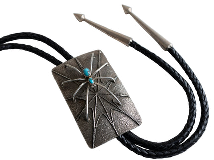 Silver Bolo tie with decorative pendant featuring a raised spider design and turquoise stone on a white background