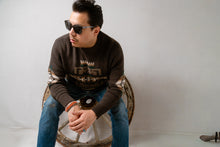 Load image into Gallery viewer, Navajo male sitting on a wooden wheel wearing Pendleton sunglasses and brown knitted sweater with blue jeans
