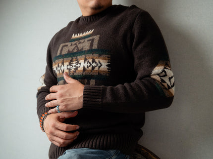 Navajo male wearing a dark brown sweater with Chief Joseph pattern, standing against a plain background