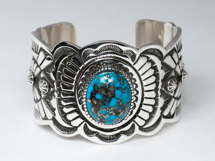A silver-stamped cuff bracelet featuring a central Persian turquoise gemstone, with intricate hand-stamped designs around it.