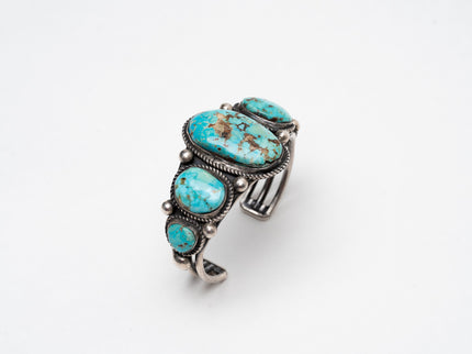 Right top view of a Native American bracelet bracelet with one large turquoise stone in the center with 2 more smaller turquoise stones on each side on a white background