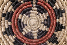 Load image into Gallery viewer, Close-up of a woven basket with concentric circle pattern in earthy tones.
