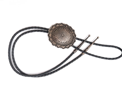 Vintage Navajo silver bolo tie with black braided cord on a white background
