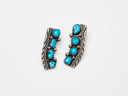 Pair of Native American silver stamped earrings with turquoise stones on a white background