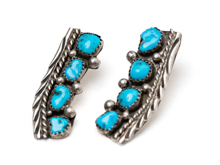 Close up of a pair of old-fashioned Native American silver stamped earrings with turquoise stones on a white background