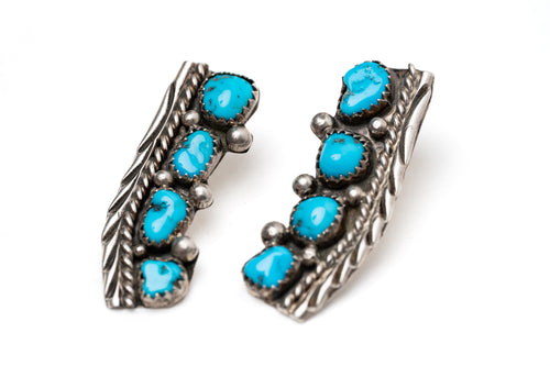 Close up of a pair of old-fashioned Native American silver stamped earrings with turquoise stones on a white background