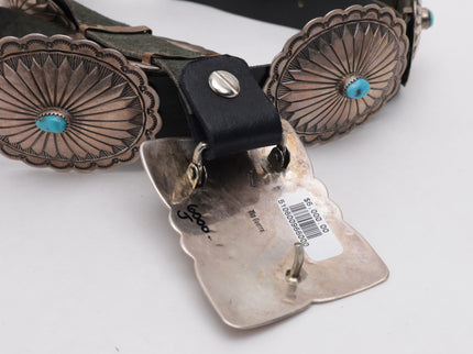 Close-up of a belt with concho details and a visible brand label on a white background