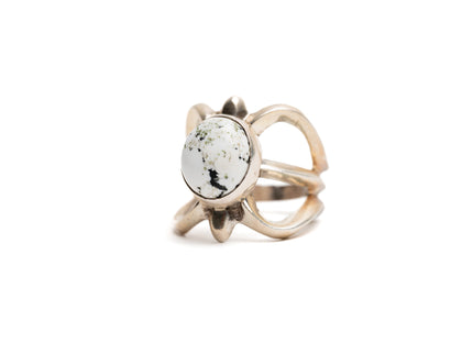 Silver cast cut-out ring showcases a single, centrally set round white buffalo stone. Ring appears gold because of the natural patina