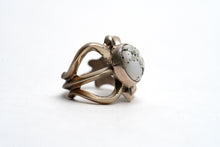 Load image into Gallery viewer, Profile view of silver cast cut-out ring showcases a single, centrally set round white buffalo stone on a white background. Ring appears gold because of the natural patina
