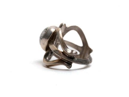 Side view of silver cast cut-out ring showcases a single, centrally set round white buffalo stone. Ring appears gold because of the natural patina