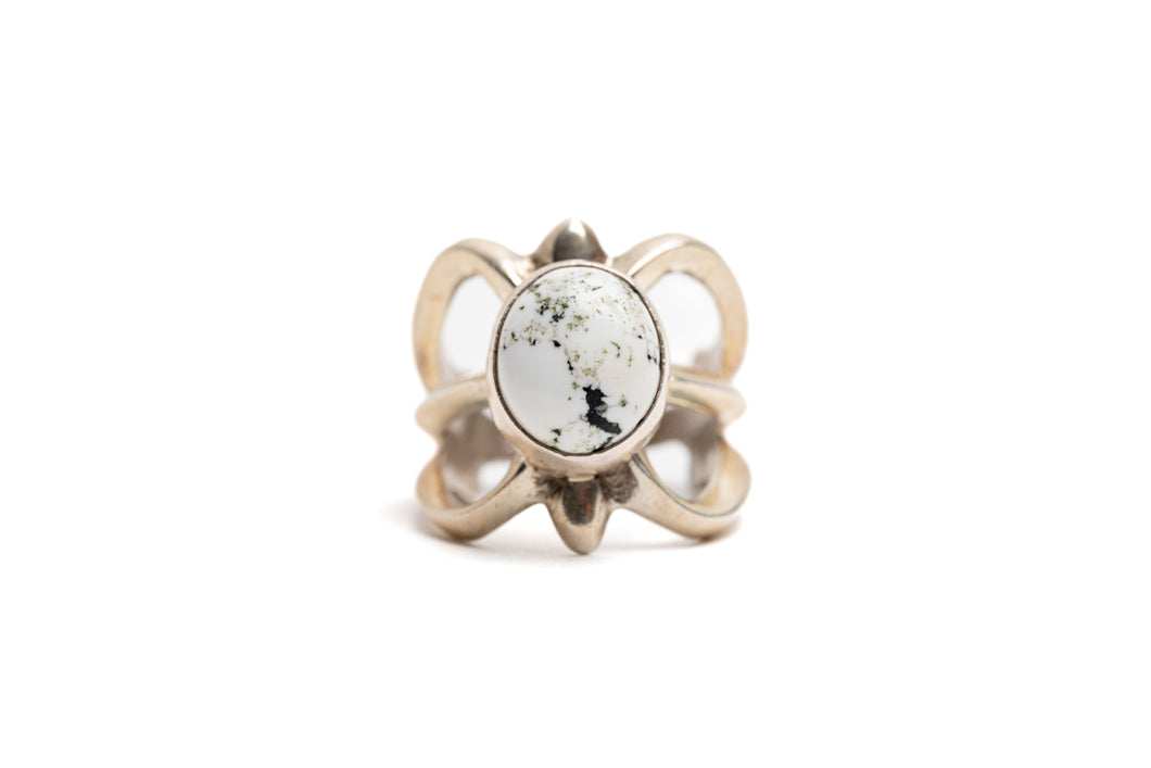 Silver cast cut-out ring showcases a single, centrally set round white buffalo stone. Ring appears gold because of the natural patina