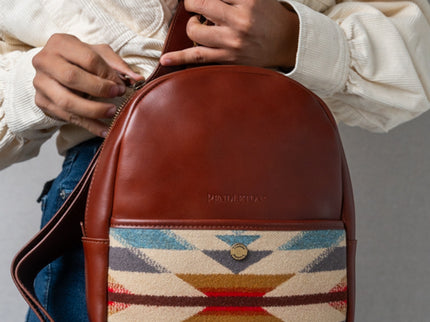 Brown leather Pendleton crossbody bag with woven pattern held by a woman wearing jeans and a creme colored button up