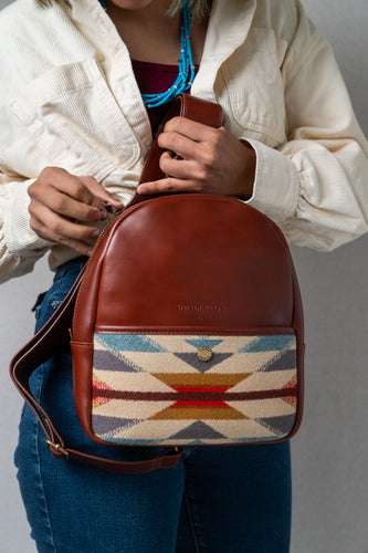 Brown leather Pendleton crossbody bag with woven pattern held by a woman wearing jeans and a creme colored button up