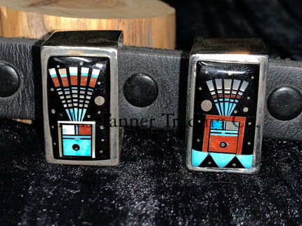 A handcrafted Ranger belt buckle set featuring intricate inlay work. two keepers, the design incorporates vibrant geometric patterns with black, turquoise, coral, and white inlays, inspired by Southwestern artistry. The bold and colorful patterns are framed by polished silver, enhancing the intricate details. The set is displayed on a black leather belt, resting on a textured dark background.
