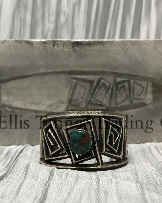 A silver Cuff with a rough silver square maze cutout. In the center is a round Royston Turquoise stone.