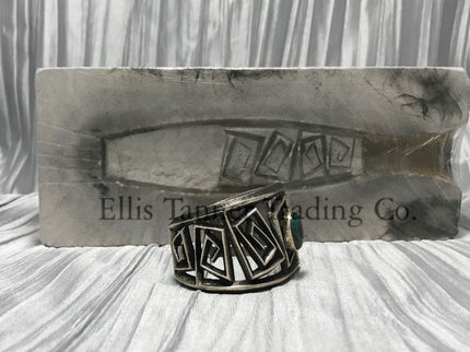 A silver Cuff with a rough silver square maze cutout. In the center is a round Royston Turquoise stone. side view 