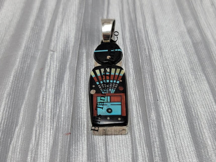 A silver pendant with a Navajo deity inlay pattern, featuring an array of colors including black, white, red, and blue.