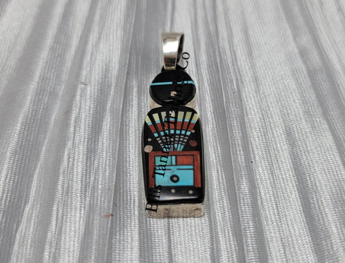 A silver pendant with a Navajo deity inlay pattern, featuring an array of colors including black, white, red, and blue.
