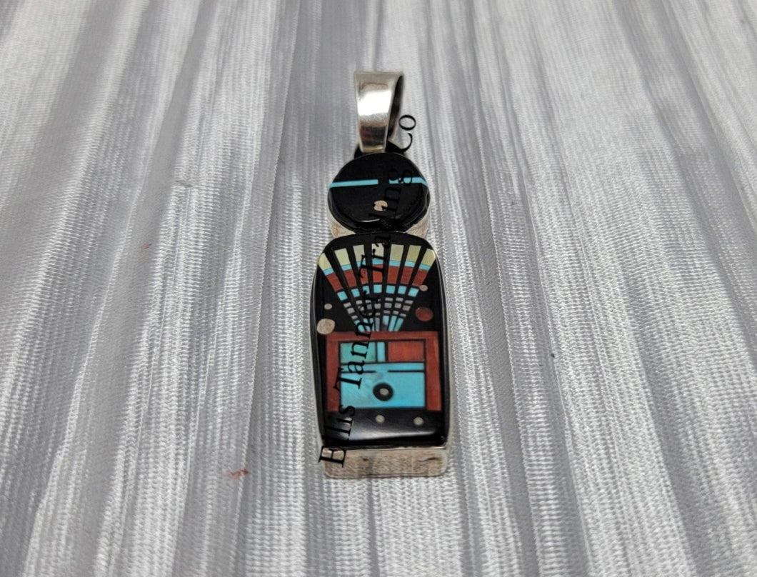 A silver pendant with a Navajo deity inlay pattern, featuring an array of colors including black, white, red, and blue.