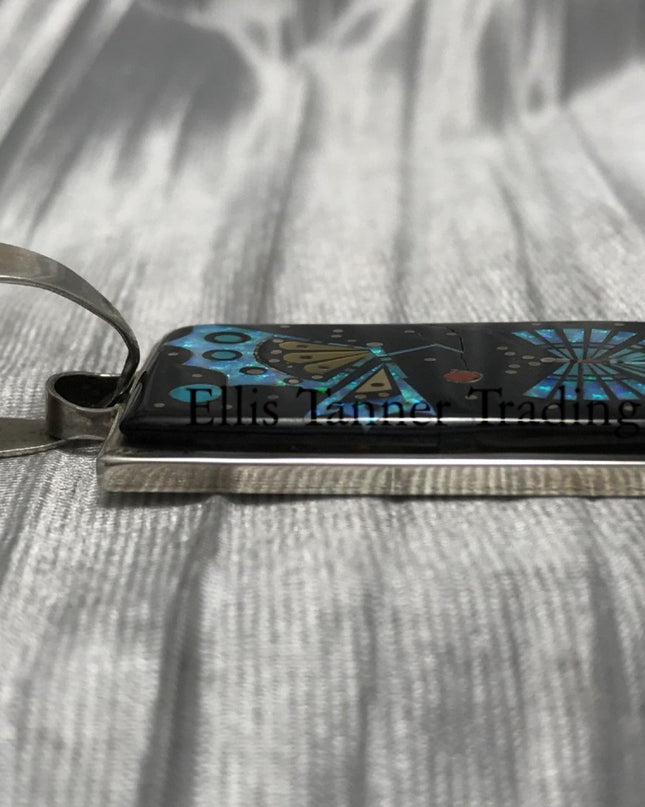 A rectangular pendant with a silver frame and loop for a chain. side view showcasing its flat inlay 