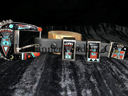 A handcrafted Ranger belt buckle set featuring intricate inlay work. The set includes a buckle, two keepers, and a belt tip. The design incorporates vibrant geometric patterns with black, turquoise, coral, and white inlays, inspired by Southwestern artistry. The bold and colorful patterns are framed by polished silver, enhancing the intricate details. The set is displayed on a black leather belt, resting on a textured dark background.