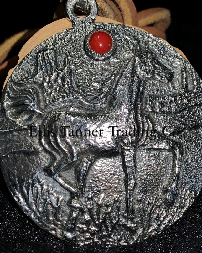 A circle silver pendant with a sand cast horse and one coral stone, with a tan leather strap. Displayed on top of a black cloth 
