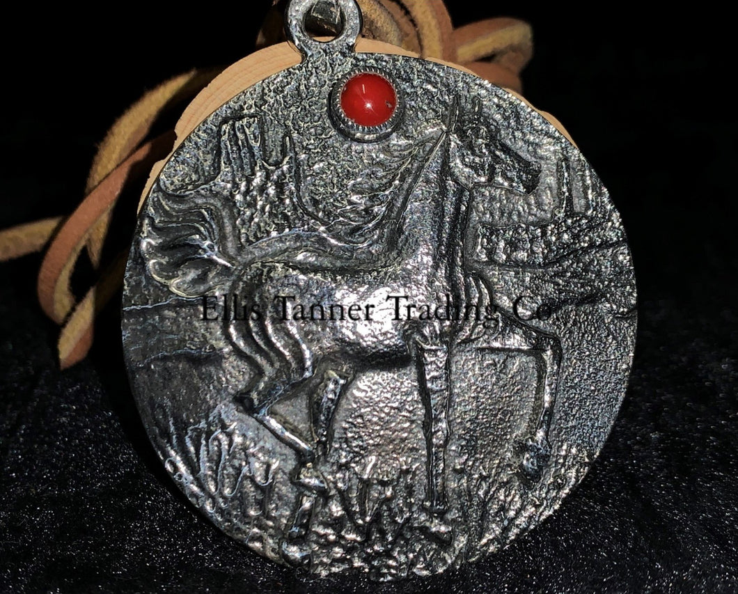 A circle silver pendant with a sand cast horse and one coral stone, with a tan leather strap. Displayed on top of a black cloth 