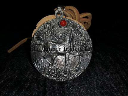 A circle silver pendant with a sand cast horse and one coral stone, with a tan leather strap. Displayed on top of a black cloth  front