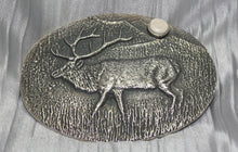 Load image into Gallery viewer, A sand-cast buckle featuring an intricately etched elk design set against a textured background. Added is a small, antler-shaped stone, adding a distinctive and natural touch. The highlighting its rustic and artisanal craftsmanship.
