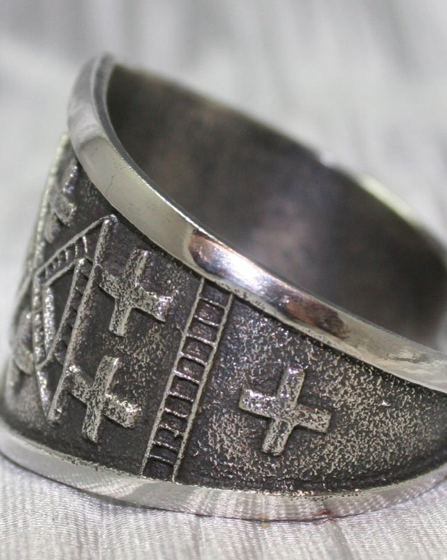 handcrafted silver cuff bracelet featuring intricate geometric and cross patterns etched into the metal. The design is bold and symmetrical, with a textured background that enhances the detailed craftsmanship. The bracelet rests on a neutral surface, emphasizing its artistic and traditional appeal.