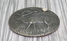 Load image into Gallery viewer, A sand-cast buckle featuring an intricately etched elk design set against a textured background. Added is a small, antler-shaped stone, adding a distinctive and natural touch. The highlighting its rustic and artisanal craftsmanship.
