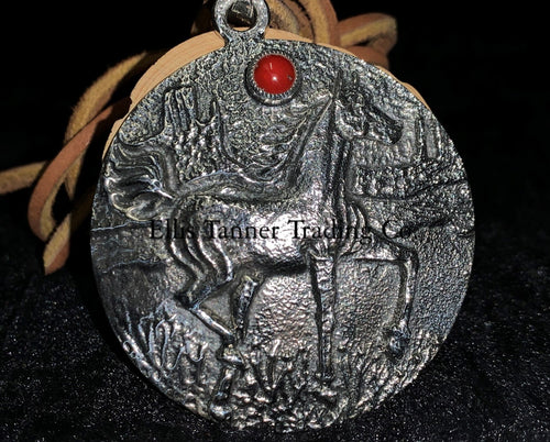 A circle silver pendant with a sand cast horse and one coral stone, with a tan leather strap. Displayed on top of a black cloth 