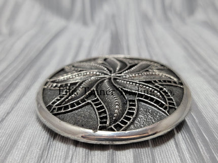 Silver sandcast, spiral flower, buckle 
 side view, placed on top of a silver cloth.