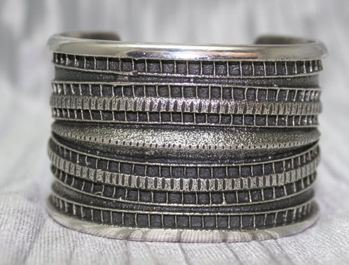 Large Sand Cast Cuff. Crafted from sterling silver using the sand cast technique, this cuff features unique texture and shine, on a shiny silver cloth.