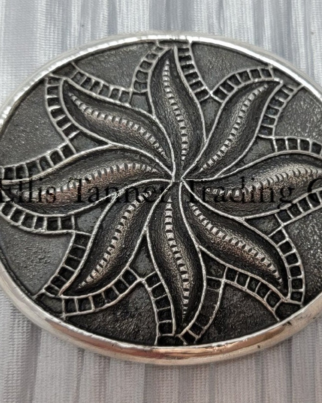 Silver sandcast, spiral flower, buckle placed on top of a silver cloth.