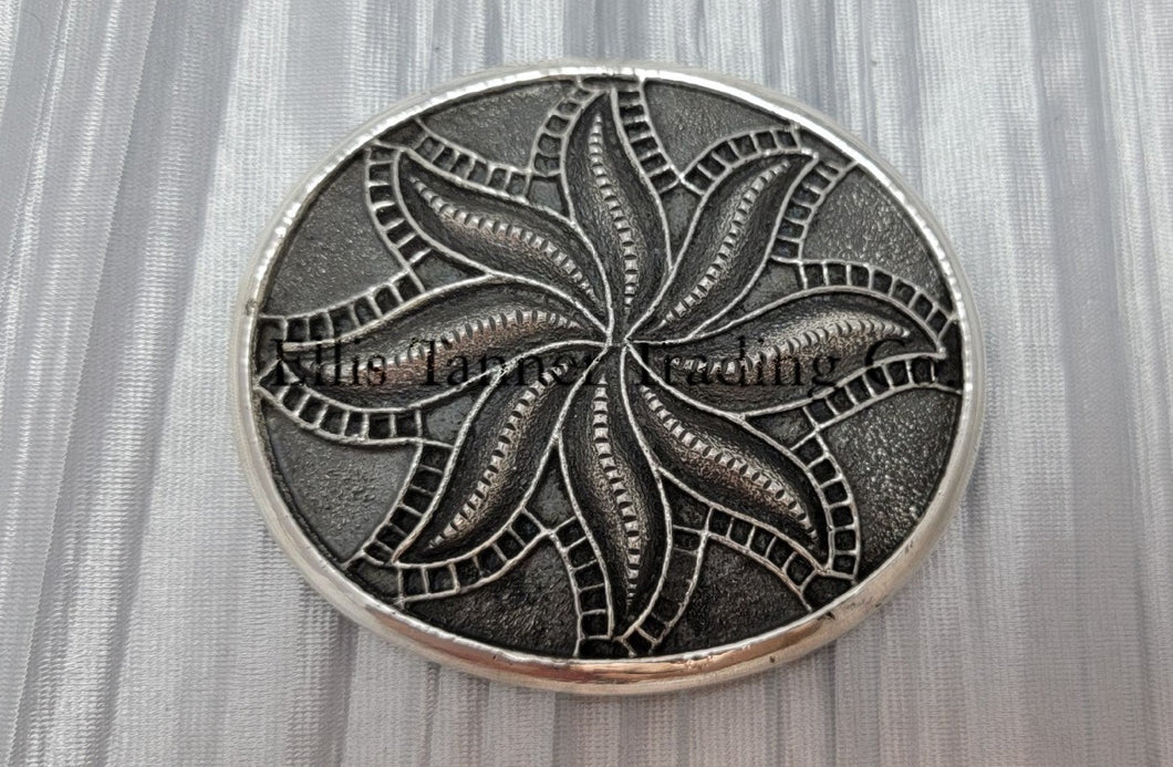 Silver sandcast, spiral flower, buckle placed on top of a silver cloth.