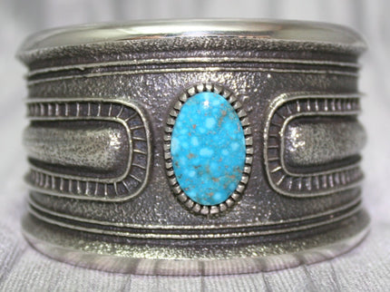 A bold sand-cast cuff featuring intricate textures and patterns, with a bright Kingman Turquoise 