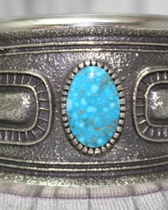 A bold sand-cast cuff featuring intricate textures and patterns, with a bright Kingman Turquoise 