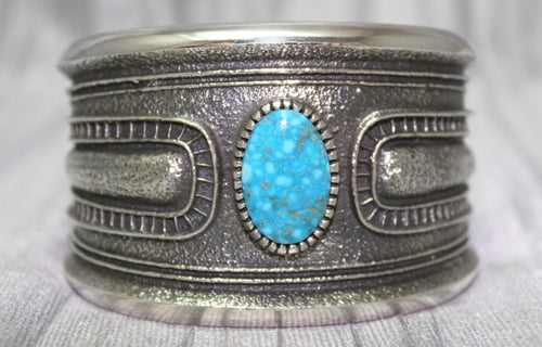 A bold sand-cast cuff featuring intricate textures and patterns, with a bright Kingman Turquoise 