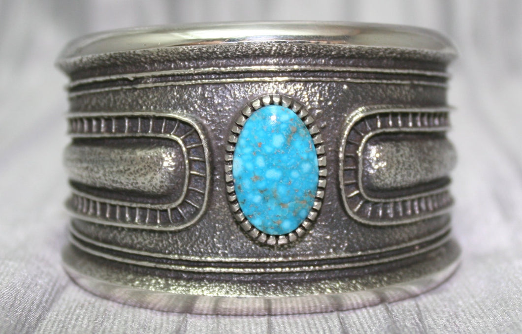 A bold sand-cast cuff featuring intricate textures and patterns, with a bright Kingman Turquoise 