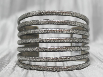 A multi-band silver cuff bracelet with a textured, rustic finish, featuring evenly spaced horizontal bands stacked in an open design. The bracelet is showcased against a soft, neutral background, emphasizing its unique craftsmanship and versatile style. 