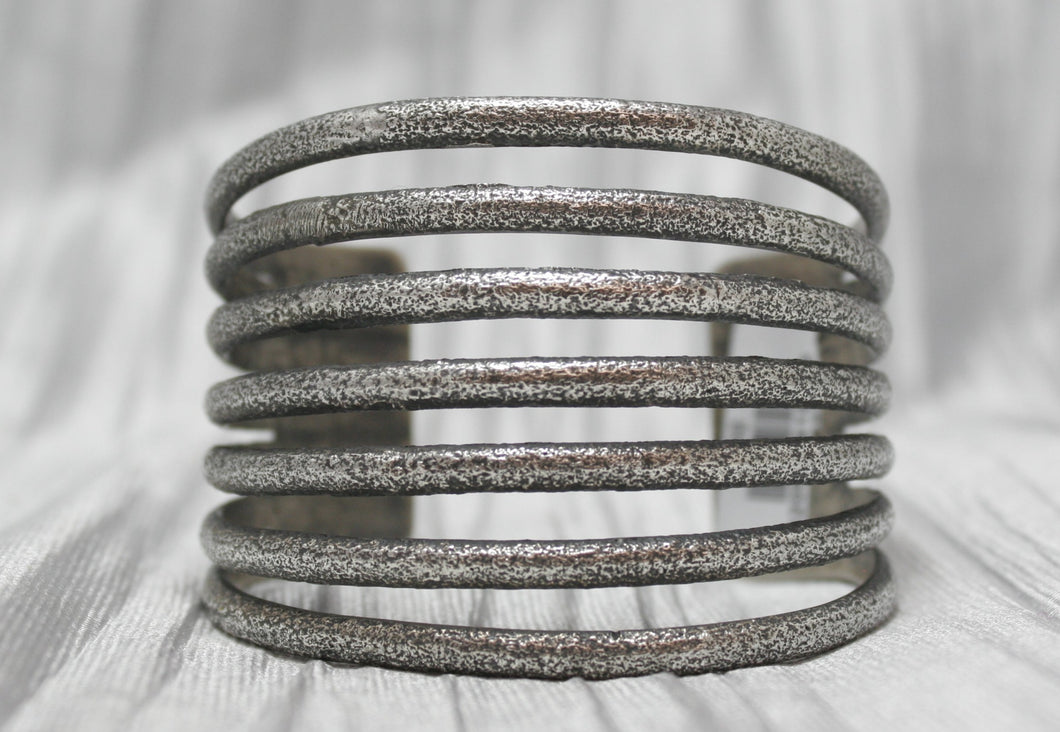 A multi-band silver cuff bracelet with a textured, rustic finish, featuring evenly spaced horizontal bands stacked in an open design. The bracelet is showcased against a soft, neutral background, emphasizing its unique craftsmanship and versatile style. 